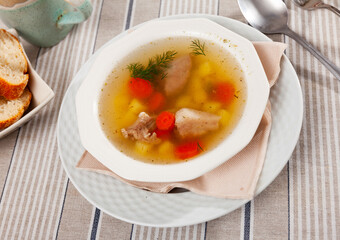 Hearty homemade soup with pork meat on bone and vegetables served with greens.