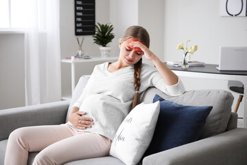 Young pregnant woman with headache sitting on sofa at home
