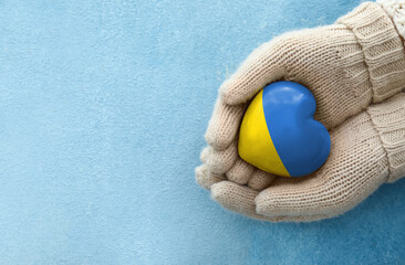 Female hands in gloves holding heart in colors of Ukrainian flag on light blue background