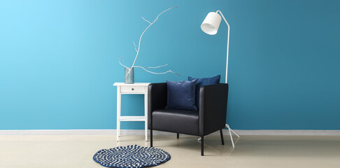 Modern armchair with table and floor lamp near blue wall