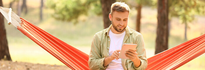 Handsome young man with tablet computer relaxing in hammock outdoors