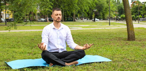 Handsome businessman meditating in summer park