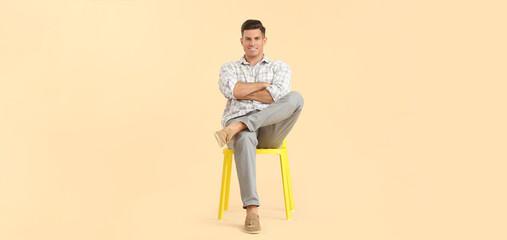 Handsome young man sitting on chair against light color background