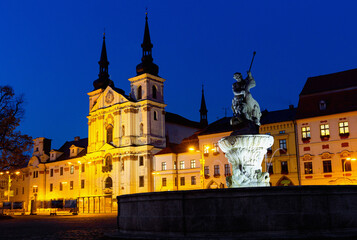 Fototapeta na wymiar View of illuminated central square of Czech city of Jihlava overlooking medieval cathedral, steeple of Town Hall and Neptune Fountain at dusk