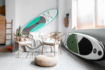 Interior of bedroom with comfortable chairs and sup surfing boards near light wall