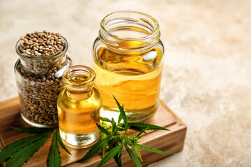 Board with bottles of hemp oil and seeds on light background, closeup