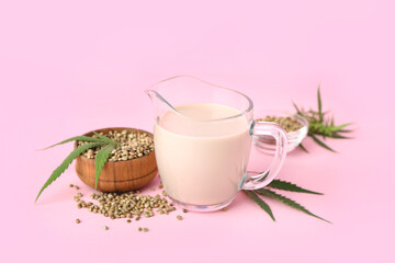 Pitcher of hemp milk and seeds on pink background