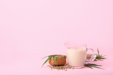 Pitcher of healthy hemp milk and seeds on pink background