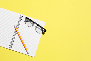 Stylish eyeglasses and notebook on yellow background