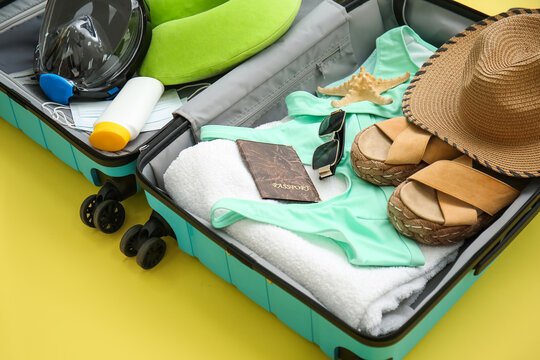Suitcase with female beach accessories and snorkeling mask on yellow background