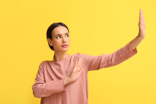 Young woman showing stop gesture on yellow background. Immunity concept