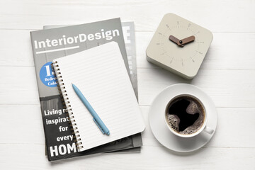 Alarm clock, magazines, notebook and cup of coffee on white wooden background