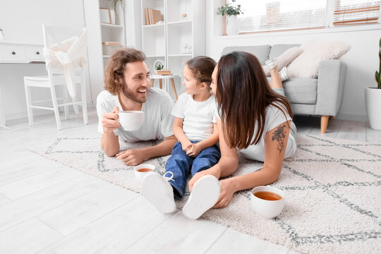 Young family with cups of tea resting on carpet at home