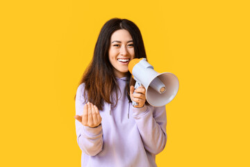 Young Asian woman with megaphone inviting viewer on yellow background