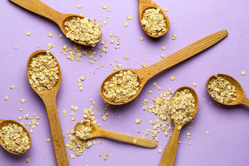 Wooden spoons with raw oatmeal on lilac background