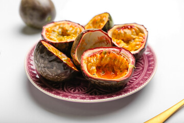 Plate with delicious cut passion fruits on white background