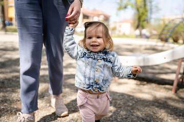 Fototapeta na wymiar One baby small caucasian child little girl in park with her mother holding hand while play in bright spring day real people childhood development learning and family concept copy space happy smile