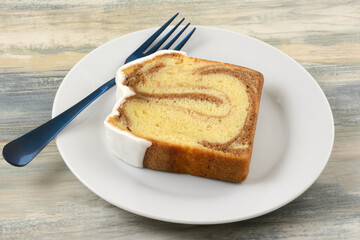 Slice of cinnamon swirl cake with icing on white plate with blue fork
