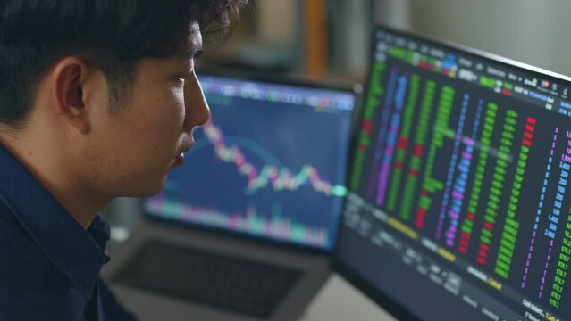 Young Asian investor man watching the change of stock market and trading stock on computer laptop screen.