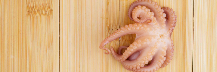 A small octopus on a wooden chopping board closeup. View from above. Copyspace © Vitaly_MOKK