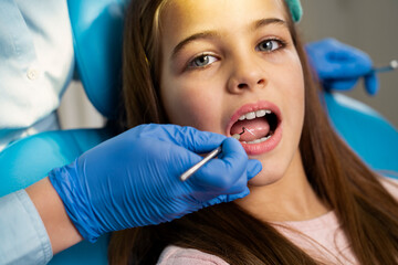 Little girl sitting in dentist chair, having routine checkup with a mirror 