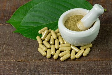 Mitragyna Speciosa Korth or kratom capsules with mortar and pestle and green leaf on rustic wooden...
