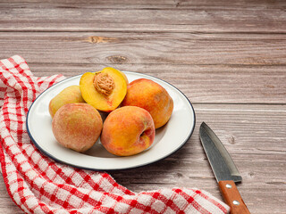 Fresh peaches fruits on a white dish, knife, and cloth on a table