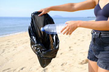 A young woman picks up trash, water bottles, plastic bottles and tons of dirt on the beach. global...