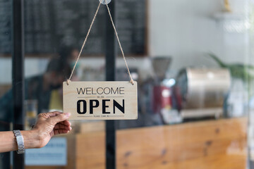 Caucasian man changes sign from closed to open at the entrance of his small coffee shop. Small business food and drink concept.