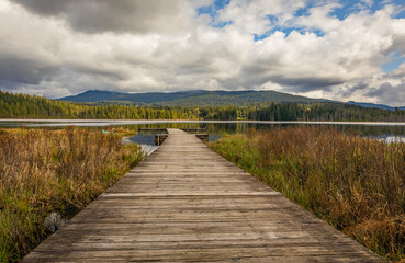 Idyllic view of a wooden pier in the lake with mountain scenery background in cloudy morning.