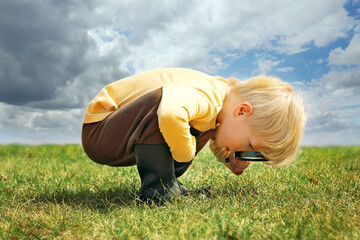 Little pre-school aged child outside looking in the grass with a magnifying glass