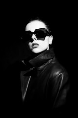 woman in leather coat and sunglasses, black background