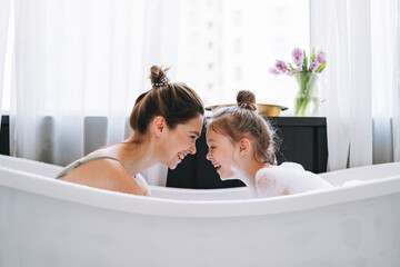 Young mother woman with long hair with little tween girl daughter in pajamas having fun in the bath...