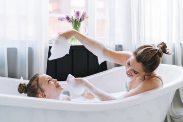 Young mother woman with long hair with little tween girl daughter in pajamas having fun in the bath...