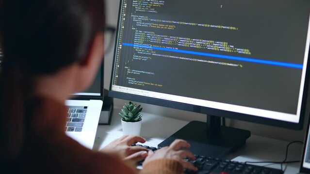 Young Asian woman, developer programmer, software engineer, IT support, wearing glasses working hard at night overtime on computer to check coding in bugging system. Back view