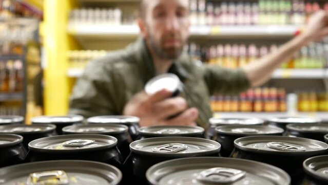 Close-up of many black cans of beer on a store shelf and a man with shopping trolley takes one