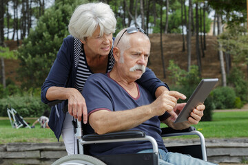 elderly couple outdoors looking at tablet man in wheelchair