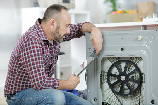 serviceman repairing washing machine looking at tablet