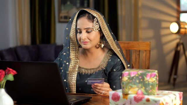 A modern Muslim woman wearing a traditional attire doing online shopping - internet connection  ATM card  a modern lifestyle. Beautifully packed gift boxes / presents kept together for Eid celebrat...