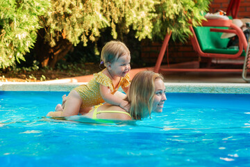 Teaching to swimming. Portrait of happy mother with her little daughter swimming in the pool. Copy space. Summer activity