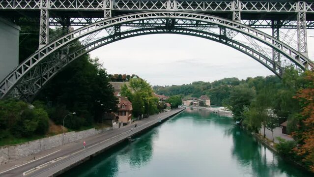 Aerial cityscape of Bern City Landmarks, Switzerland. Arch metal bridge across Aare River in Old Town with Munster Cathedral. Water transportation and Travel in Europe. 4K drone zoom in shot