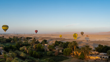 Bright balloons over Luxor. Village houses, palm trees, green vegetation are visible below. In the...