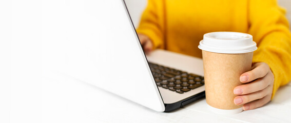 Crop view of a young business woman in a yellow sweater sitting at a table in a cafe, female using laptop and drinking coffee. Student or freelancer working online, remote workplace. Copy space.