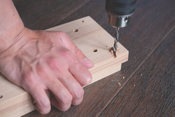 Man is drilling a hole on wooden board for production hand furniture diy at home 