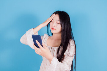 Portrait of a shocked asian woman using mobile phone on blue background