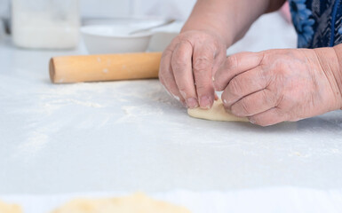 Senior woman hands making pies with apple filling on a white kitchen table with wooden rolling pin on background. Selective focus. Cooking at home concept. Tradition home-made food