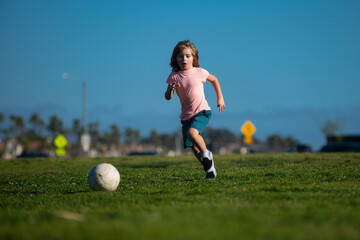 Excited child boy kicking ball in the grass outdoors. Soccer kids, children play football.