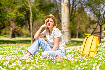 A young blonde girl in a hat enjoying spring in a park in the city, vacations next to nature and next to daisies