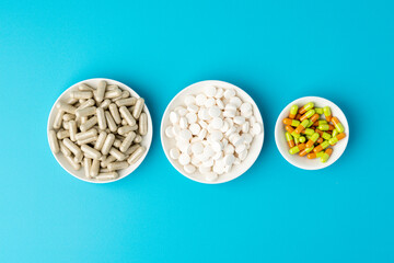 Turquoise background of large group of assorted capsules, pills and tablets in white bowls in a row