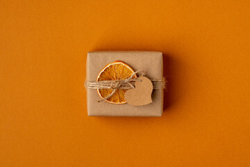 Craft gift package on orange background. Handcrafted cardboard box in wrapping paper and adornment.